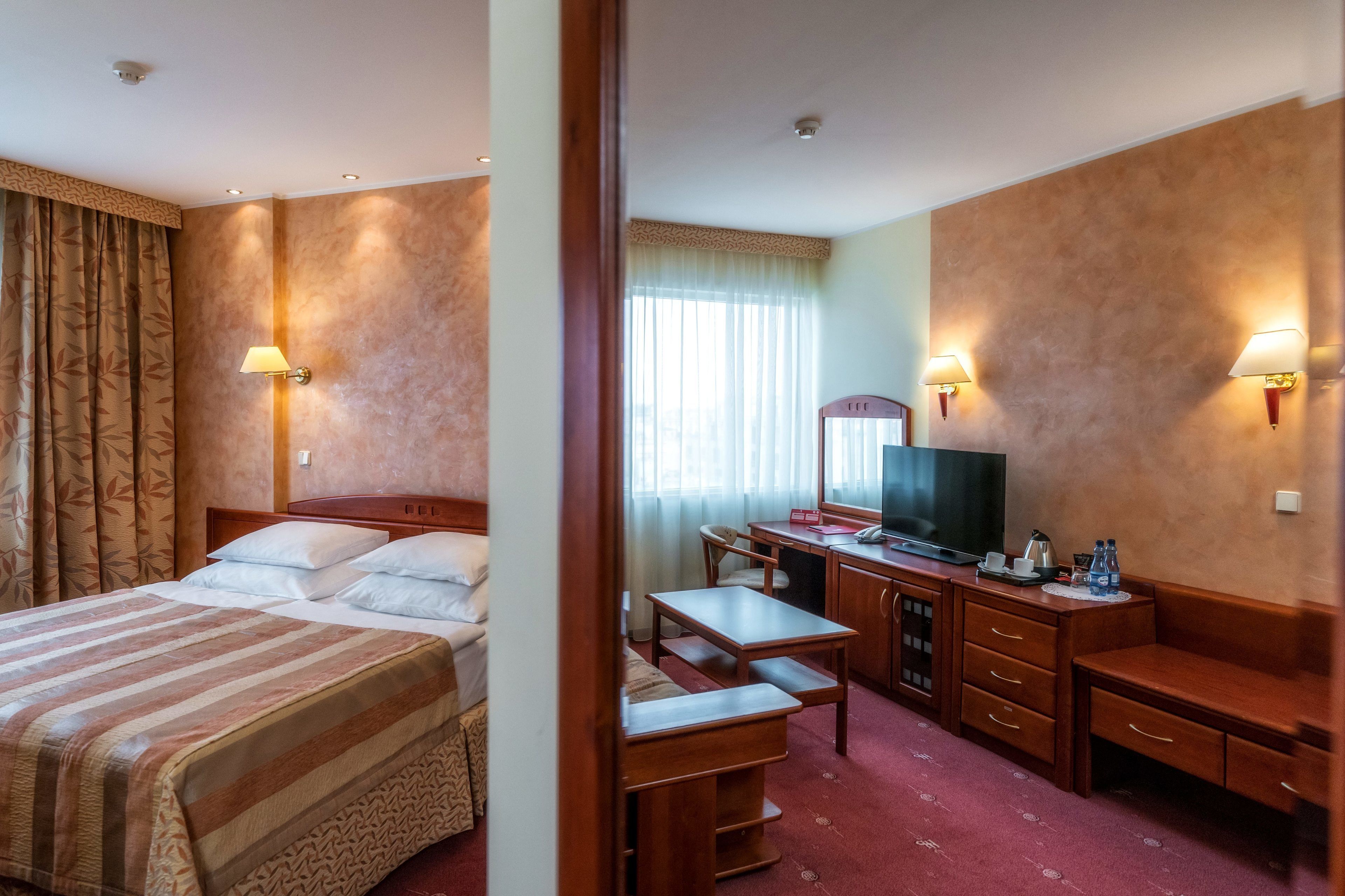 A hotel room with a bed, desk, chair, and a television.