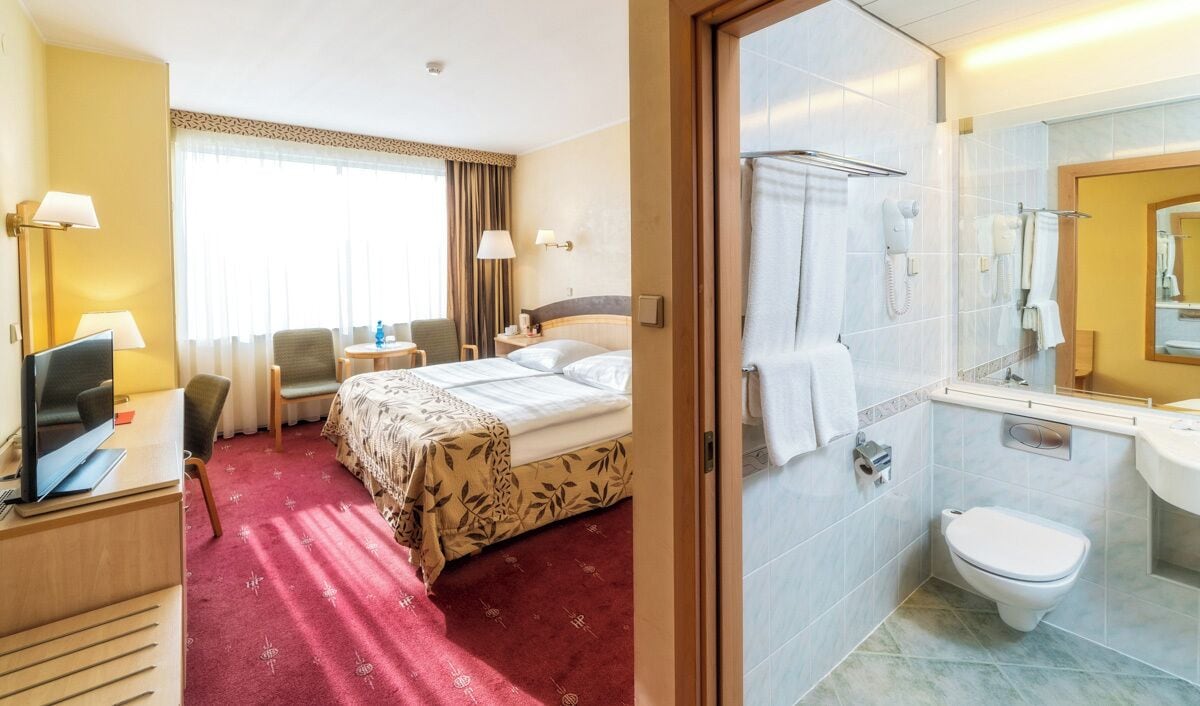 A hotel room with a bed, desk, TV, and a bathroom with a shower and toilet.