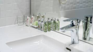 Un baño con un lavabo blanco, un espejo y distintos artículos de aseo, incluyendo botellas y un vaso.