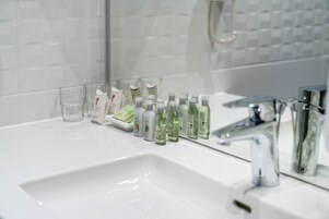 Un baño con un lavabo blanco, un espejo y distintos artículos de aseo, incluyendo botellas y un vaso.