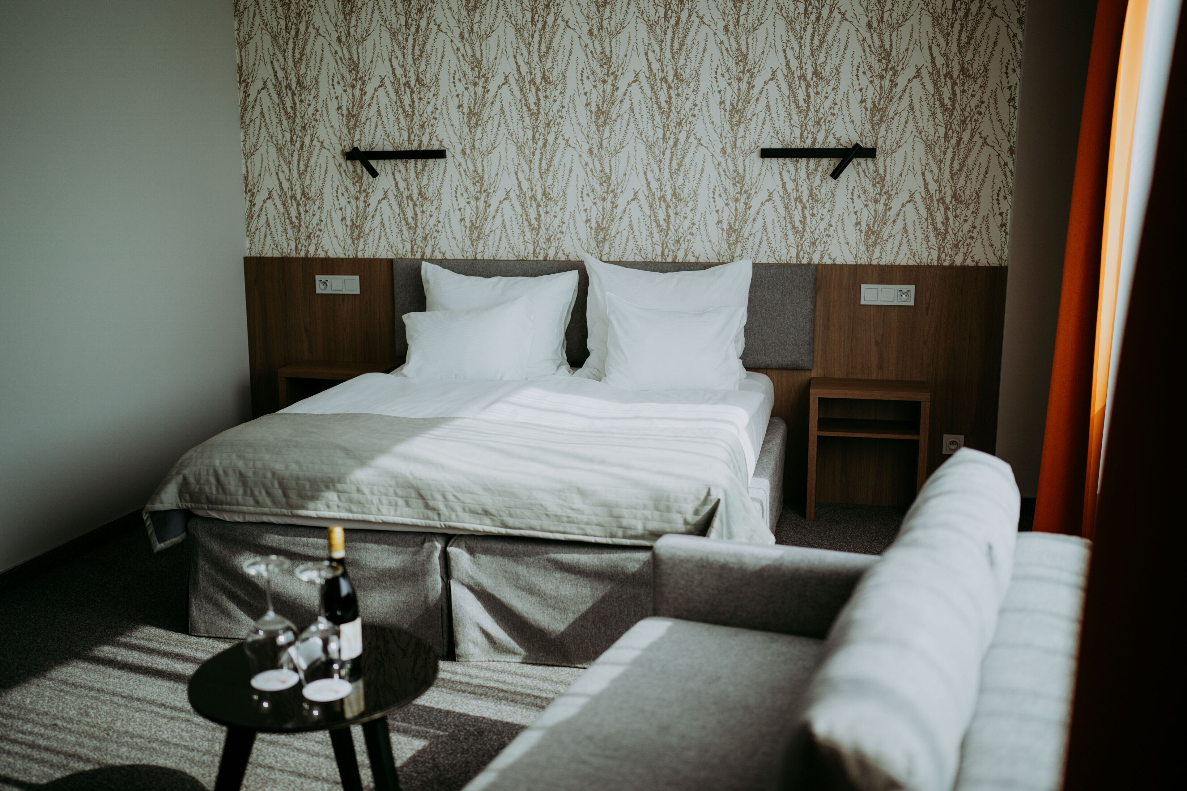A hotel room with a bed, a small table with a bottle and glass, and a sofa.