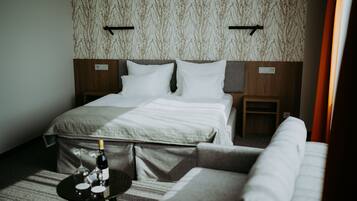 A hotel room with a bed, a small table with a bottle and glass, and a sofa.