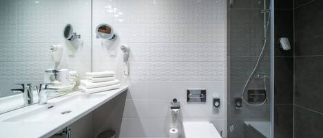 Un baño moderno con lavamanos blanco, inodoro, ducha con mampara de vidrio y toallero.