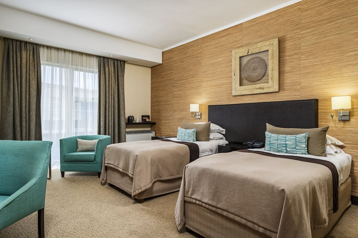 A hotel room with two beds, a sofa, a coffee machine, and a wall-mounted picture.