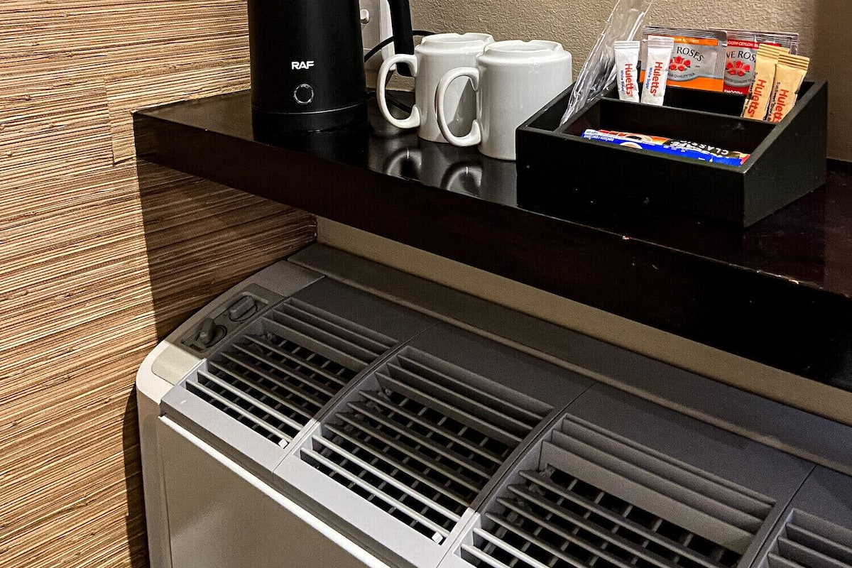 A coffee station with a black coffee maker, white mugs, and a tray of coffee packets.