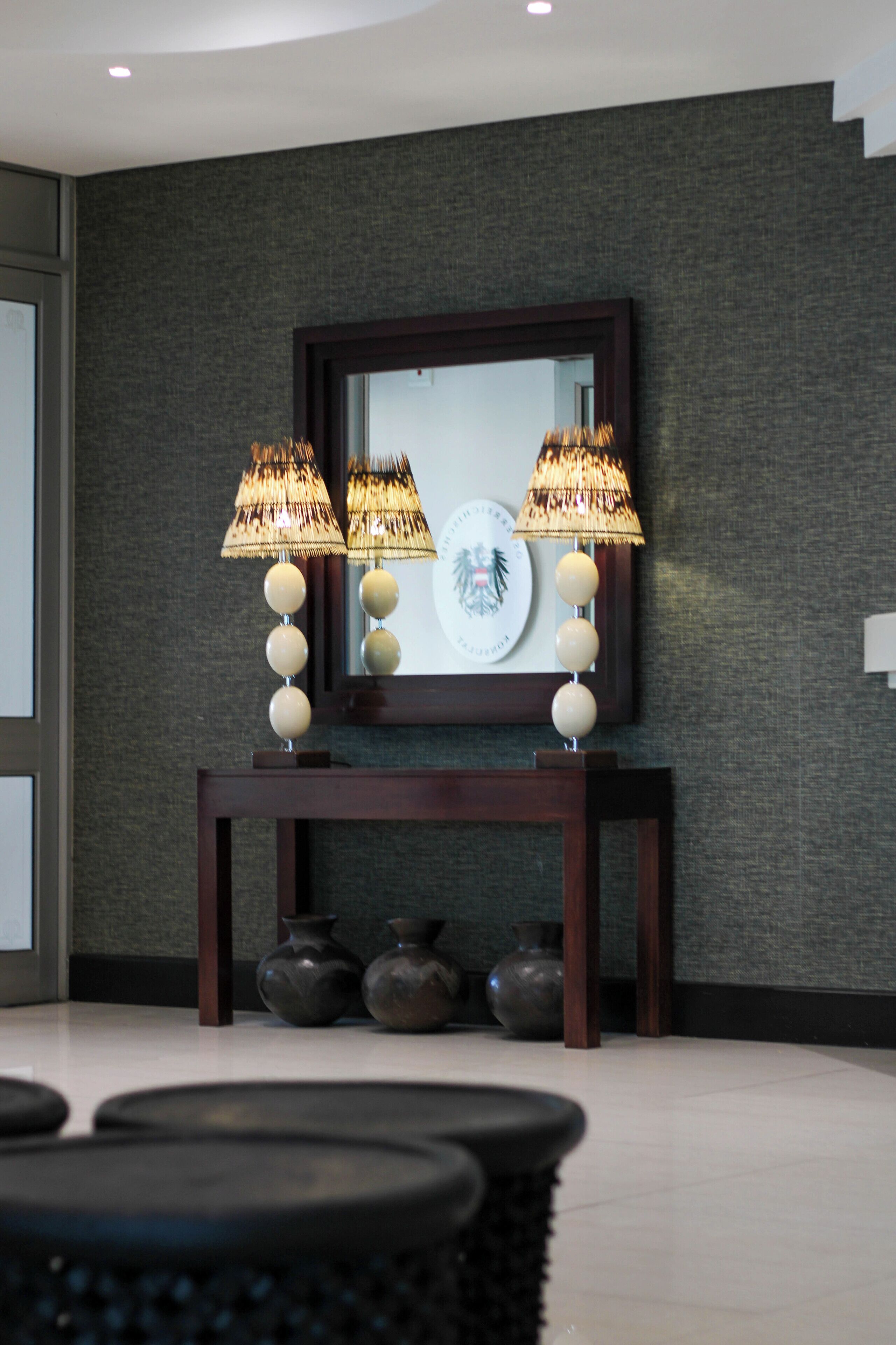 A modern interior with a dark textured wall, a wooden console table, two wall-mounted lamps, and three vases.