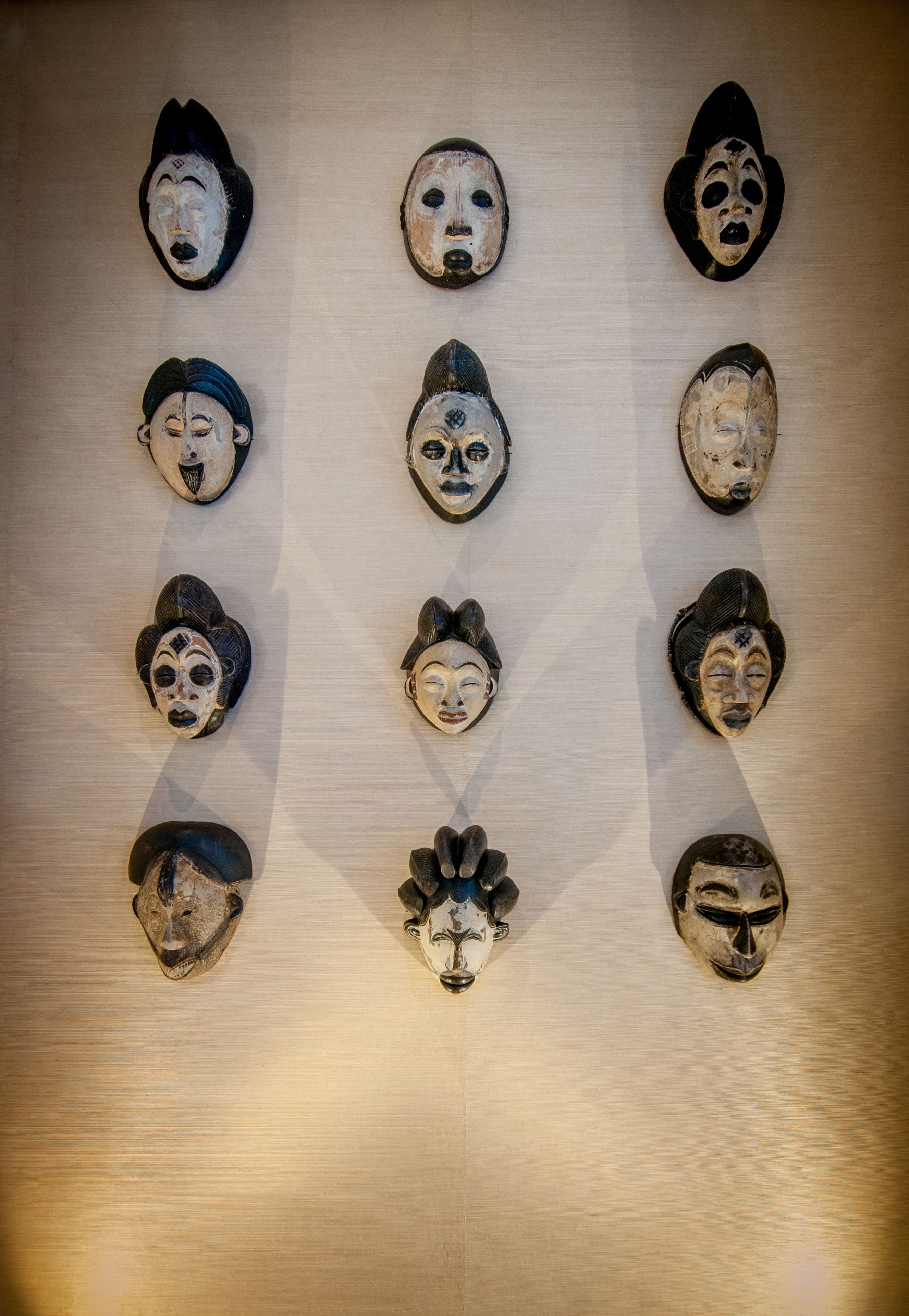 A collection of wooden masks arranged in a grid pattern on a wall.