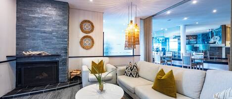 A modern living room with a fireplace, a sofa, a coffee table, and a large window offering a view of the interior.