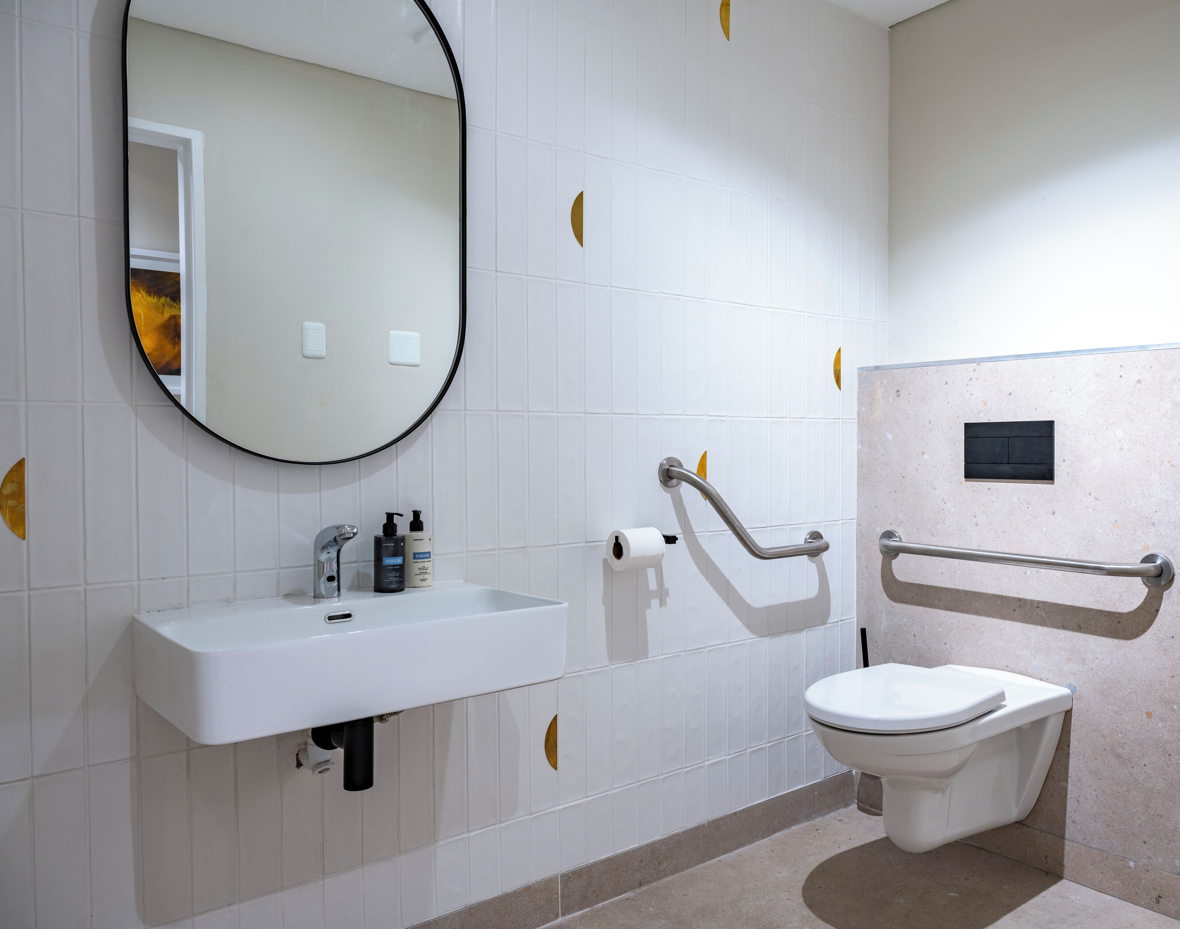 A bathroom with a white sink, a toilet, a mirror, and grab bars.