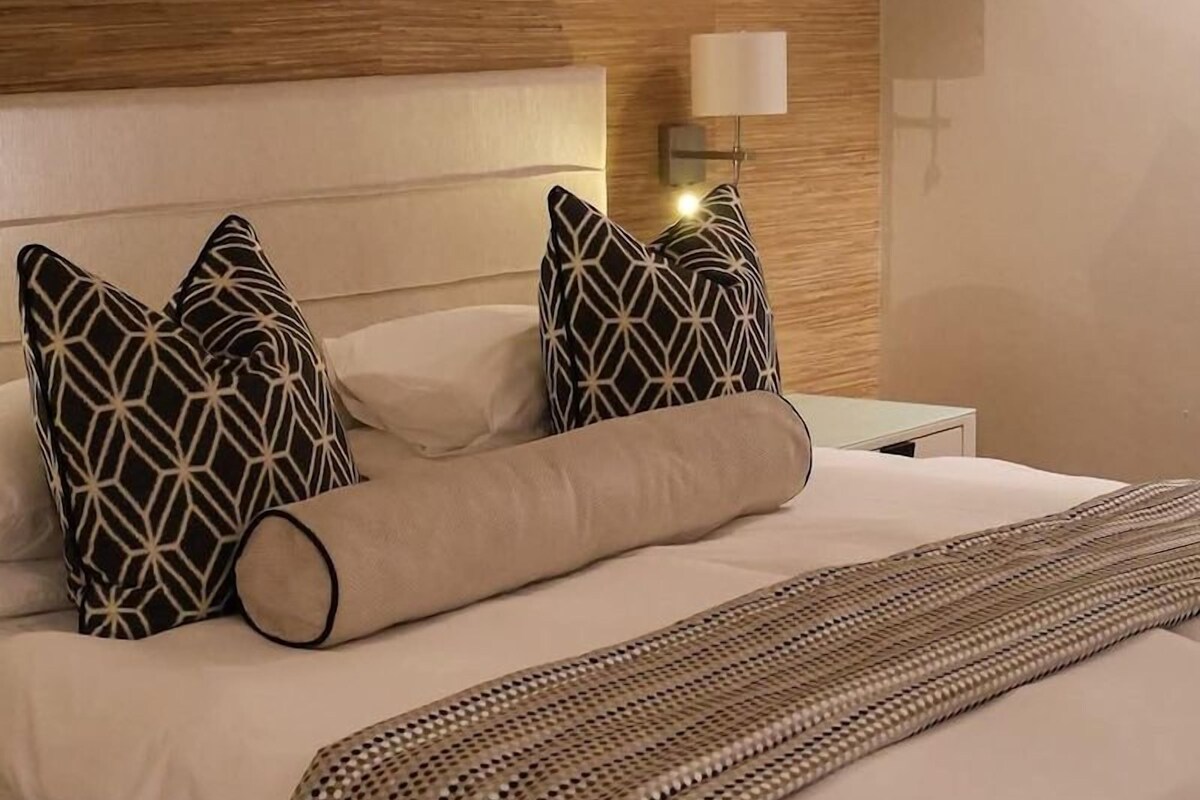 A neatly made bed with patterned pillows, a woven throw, and a wooden headboard.