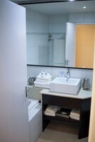 A compact bathroom with a white sink, a mirror, a towel rack, and a shower area.