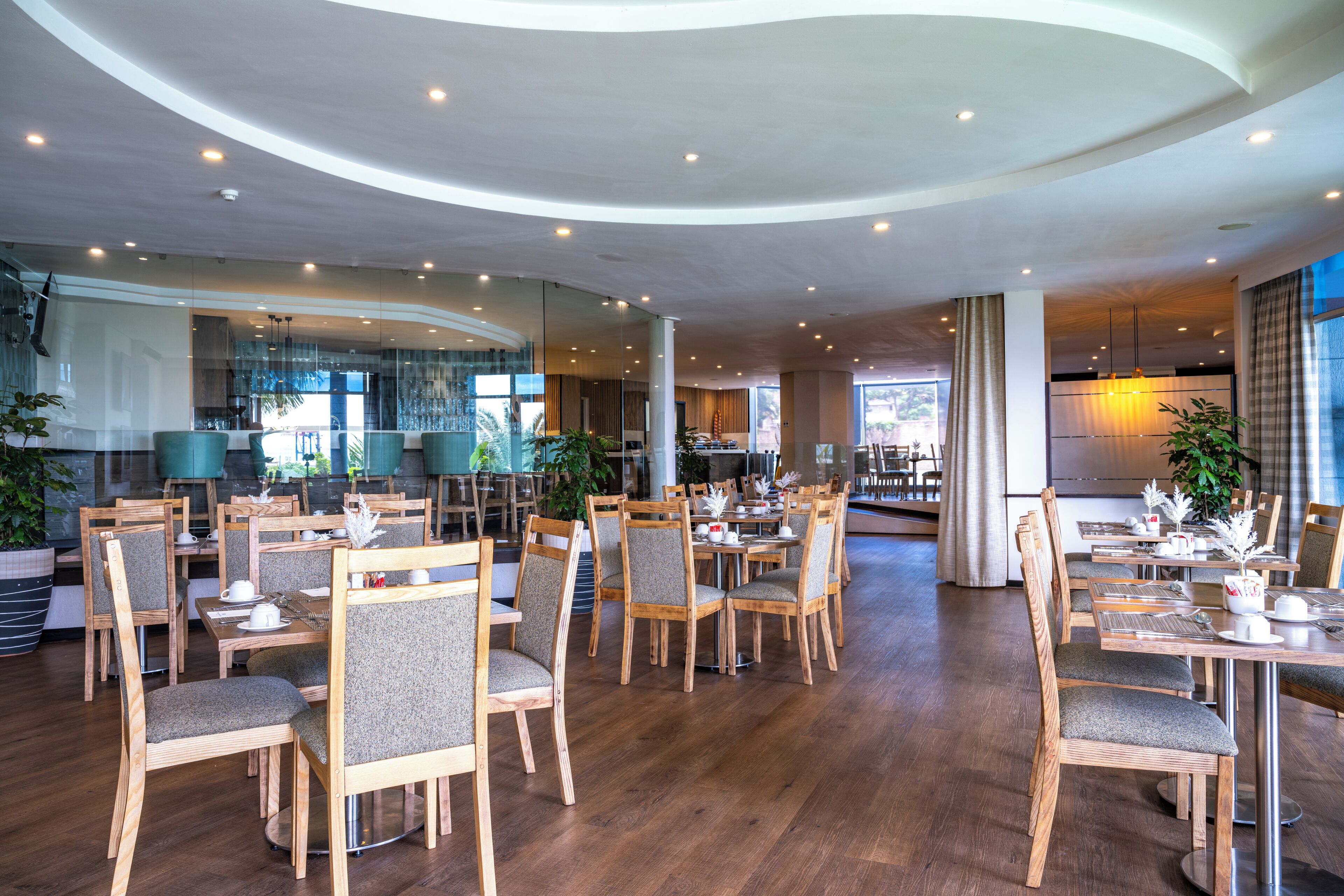 A spacious dining area with wooden tables and chairs, large windows, and modern lighting.