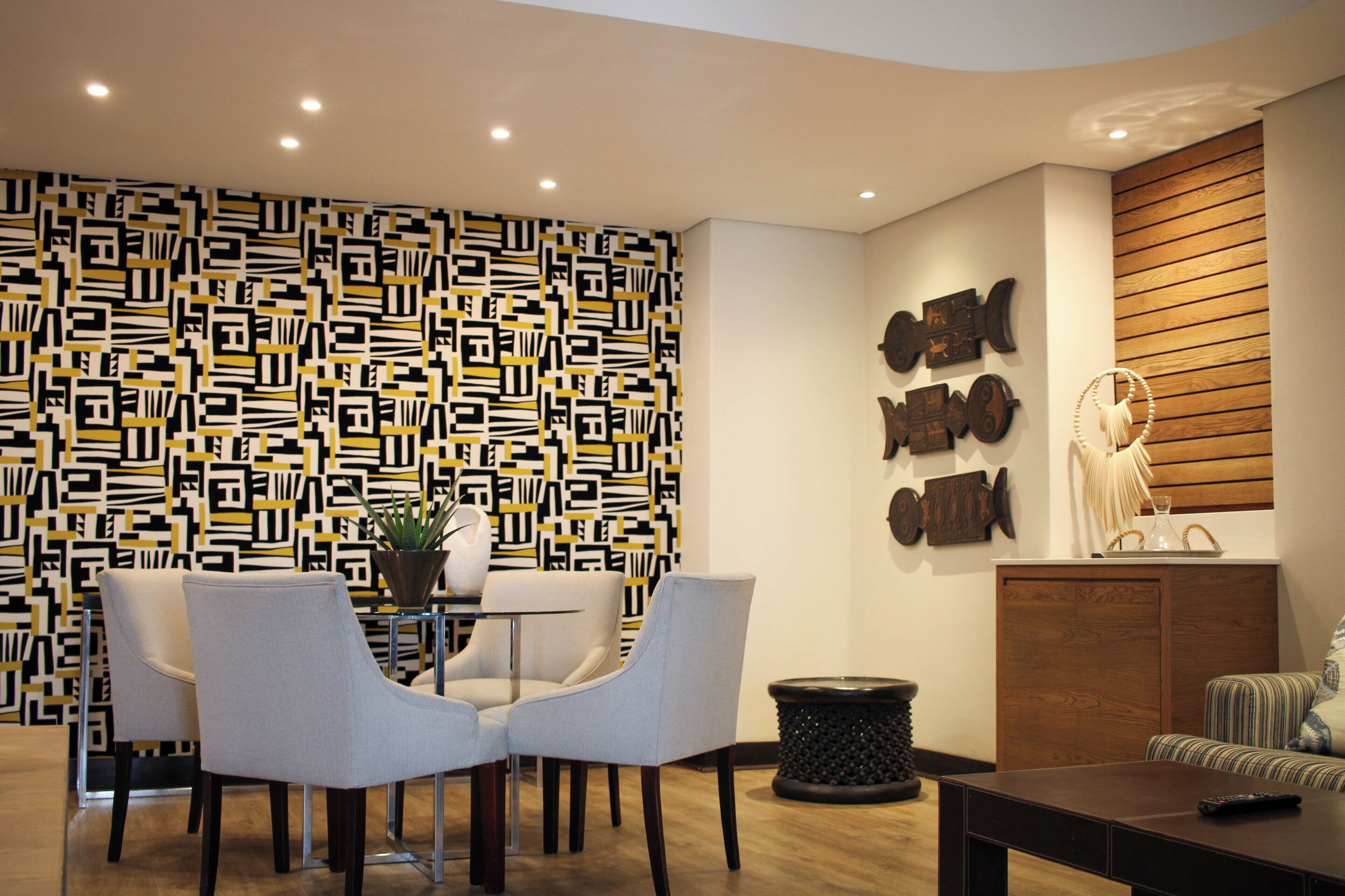 A modern living room with a geometric patterned wall, a wooden panel wall, and a dining area with chairs and a table.