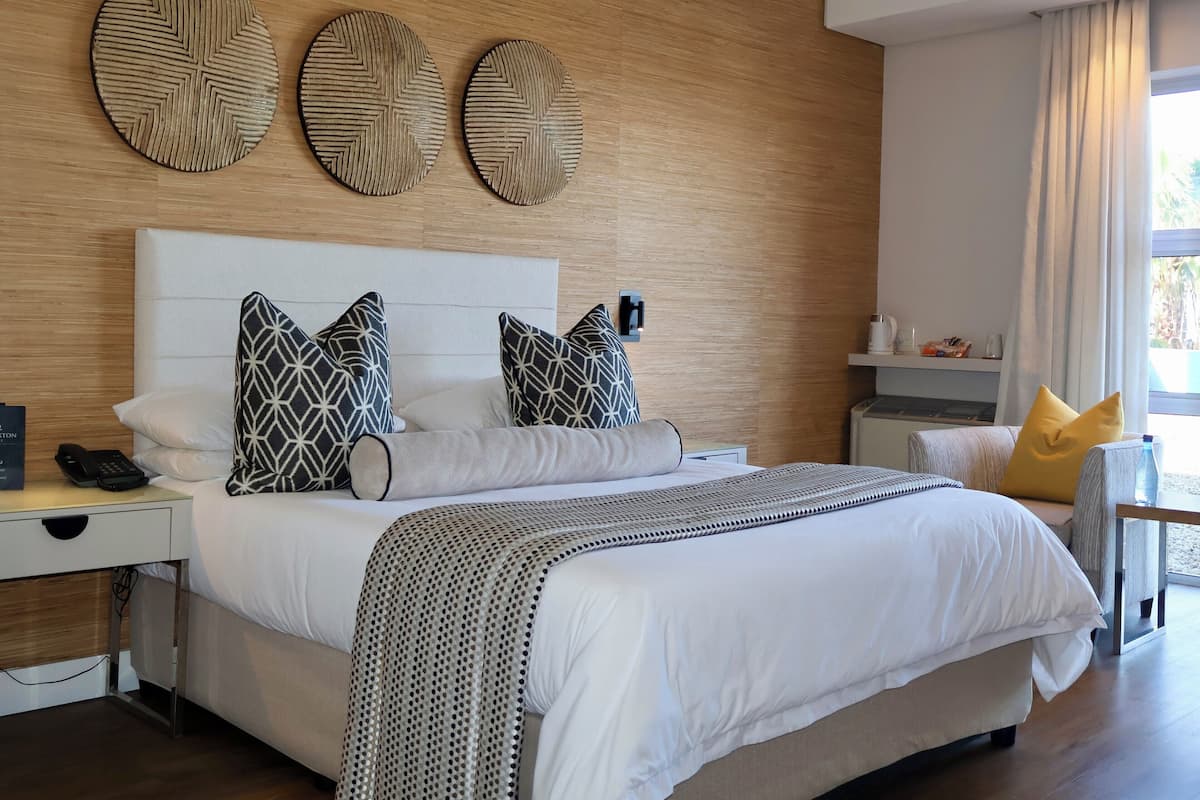 A modern hotel room with a large bed, a bedside table with a phone, and a nightstand. There are three wall-mounted clocks above the bed.
