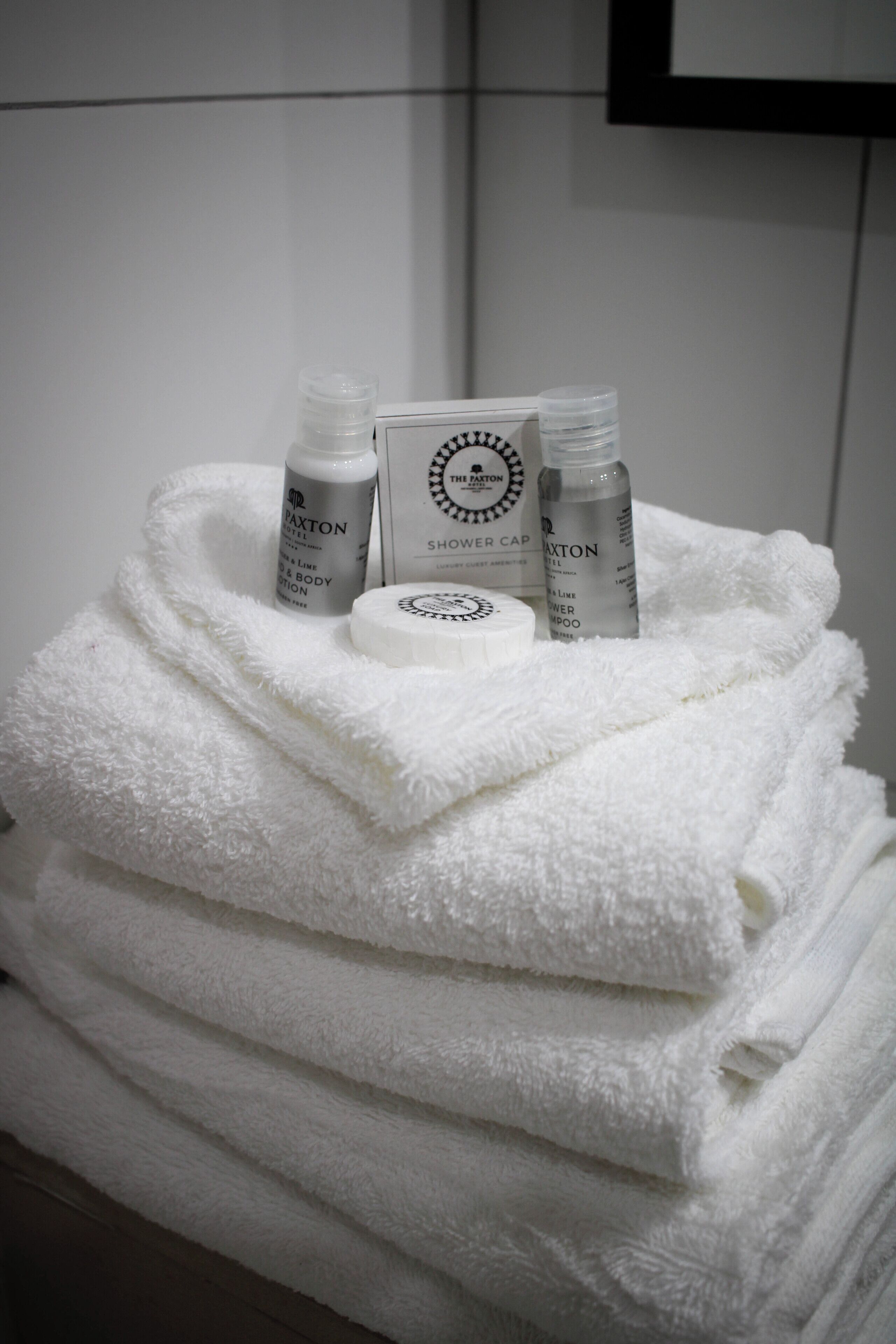A stack of white towels with a bottle of body lotion and a shower cap on top.