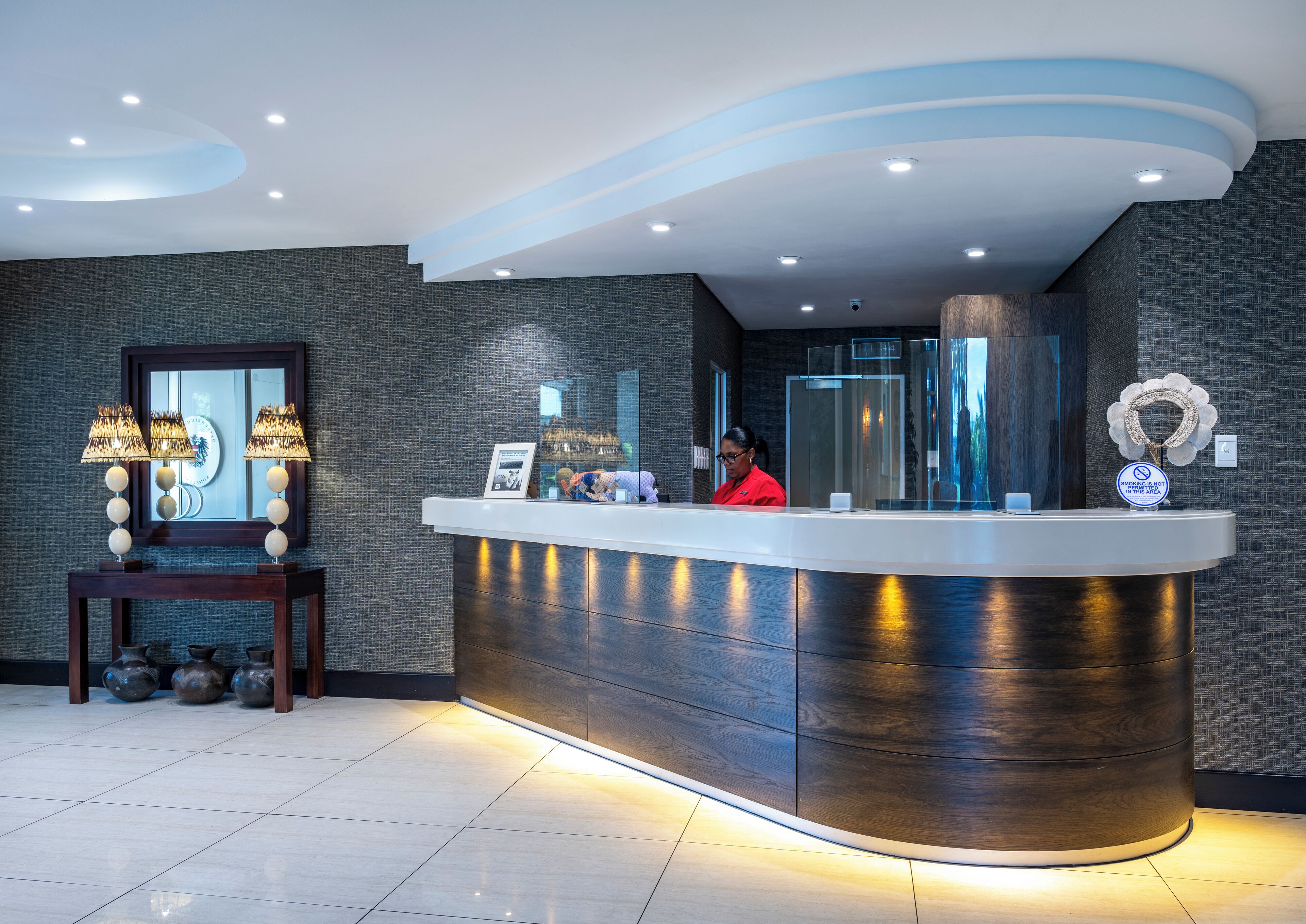 A reception desk with a modern design, a receptionist, and a decorative wall with a mirror and framed picture.