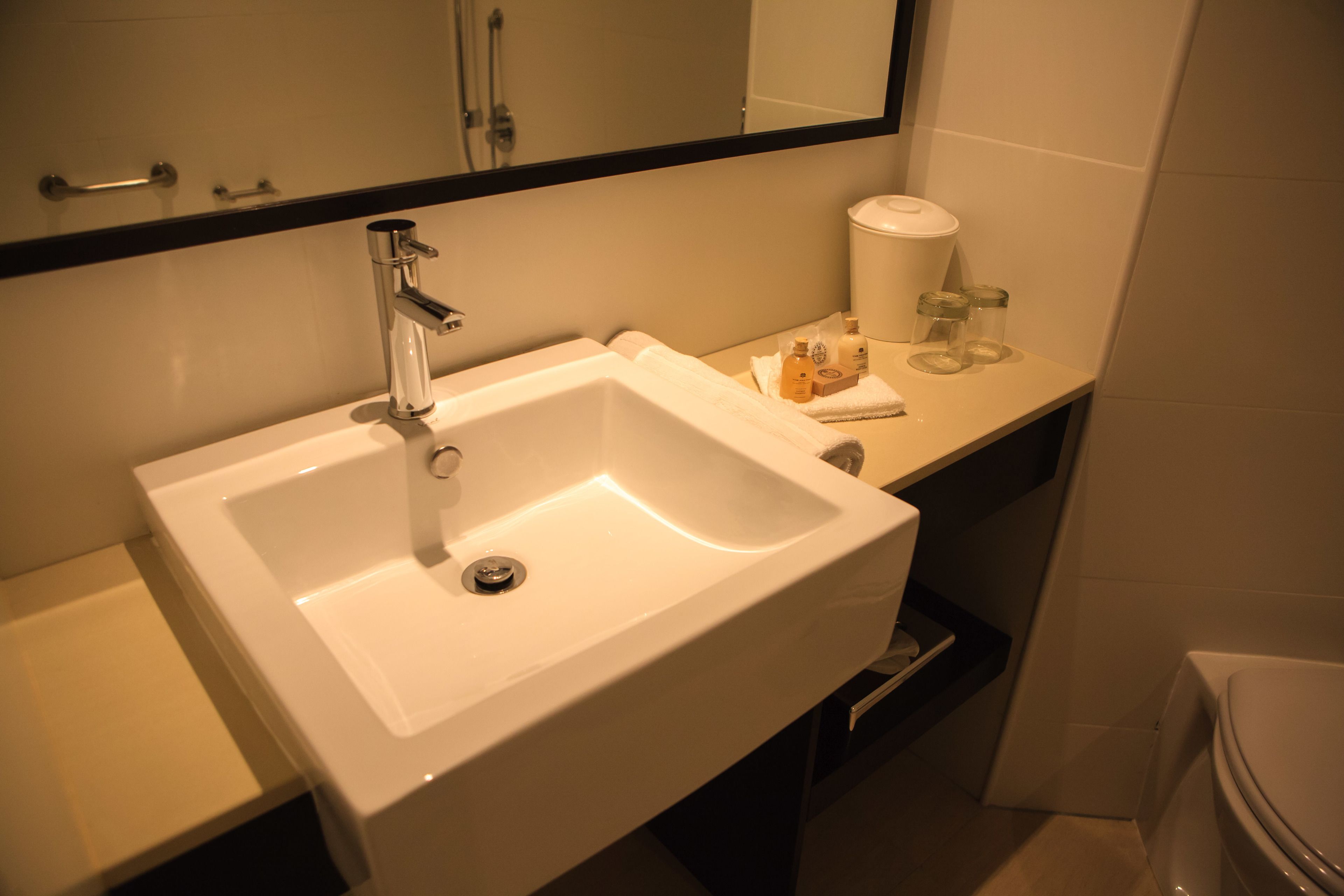 Un baño con un lavabo blanco, un espejo encima y un inodoro a la derecha.