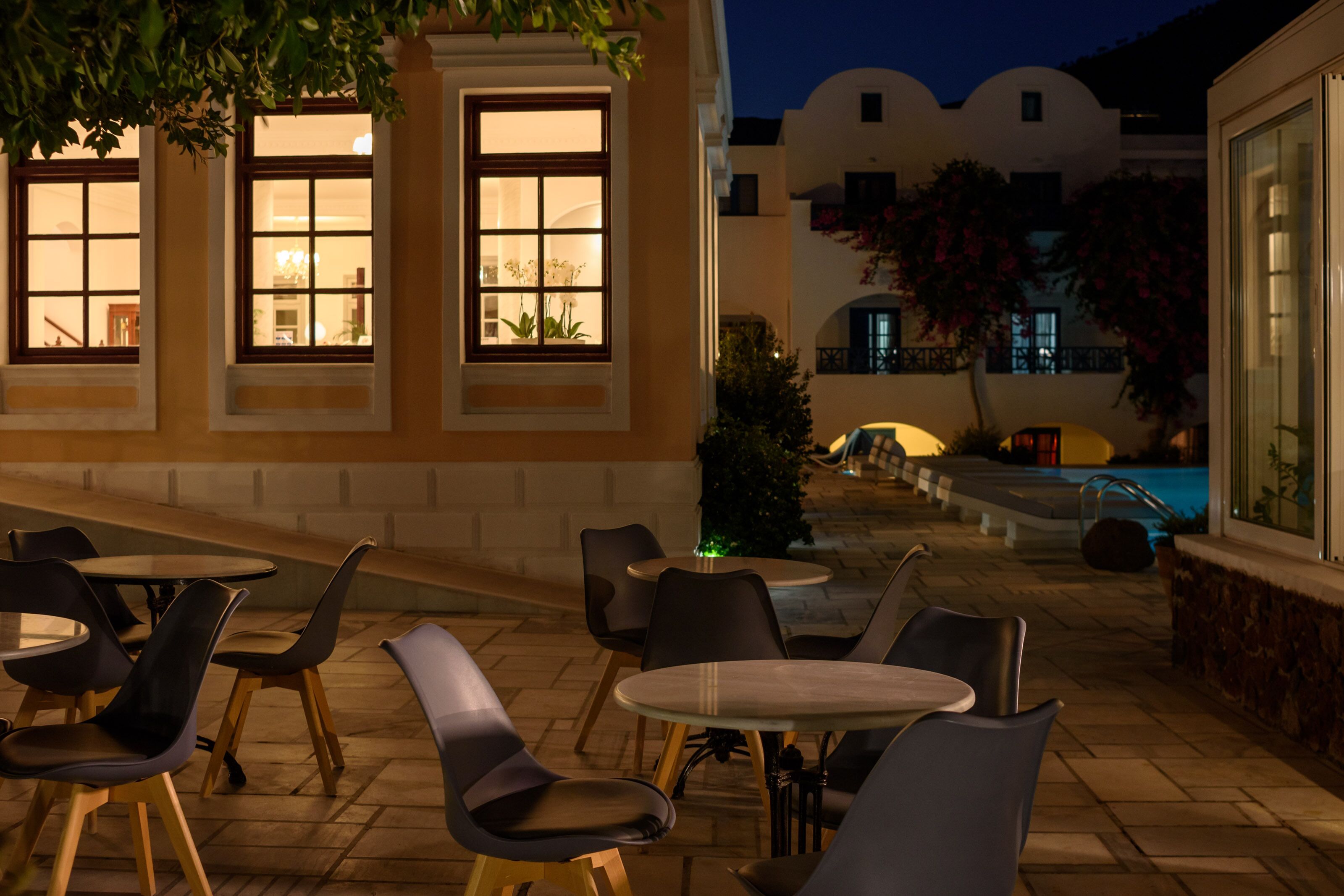 An outdoor patio with tables and chairs, a swimming pool, and a building with large windows.