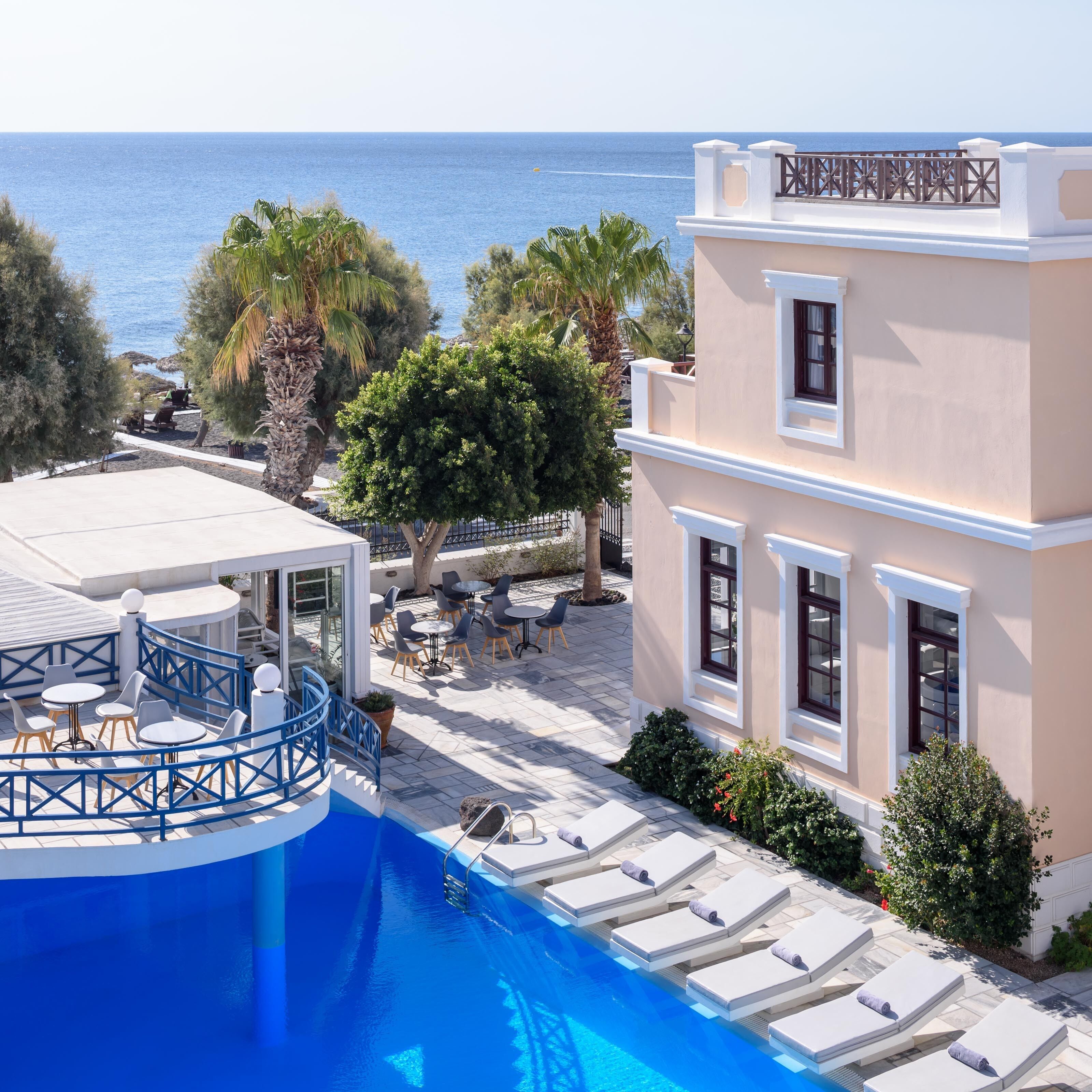 A poolside area with lounge chairs and a pool, overlooking the sea.