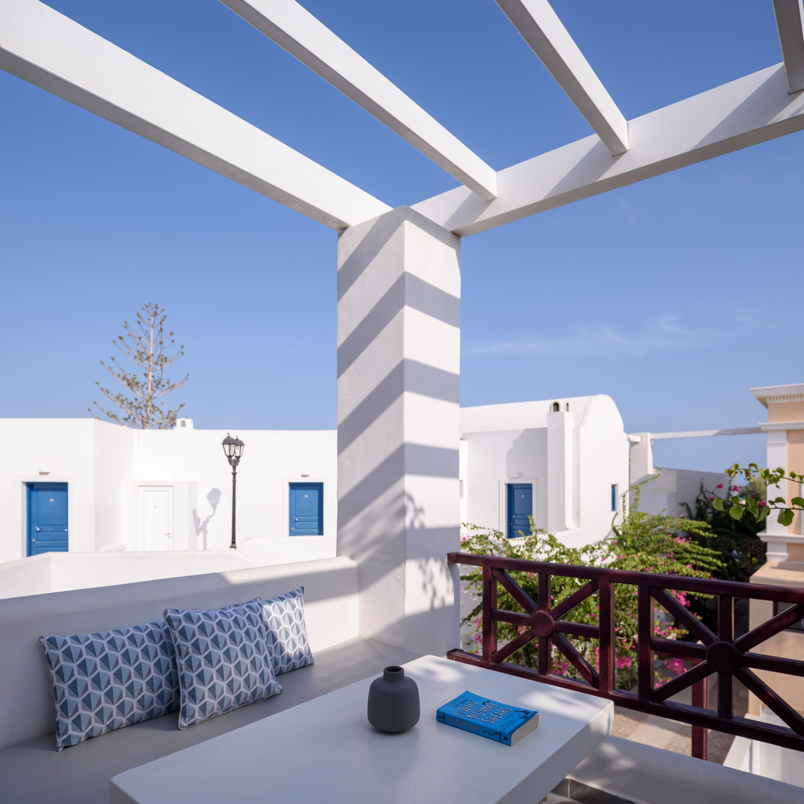 A white-walled room with a blue door, a white table with a book and a vase, and a view of the sky.