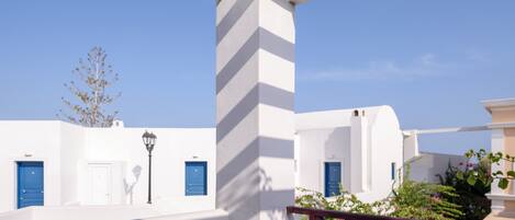 A white-walled room with a blue door, a white table with a book and a vase, and a view of the sky.