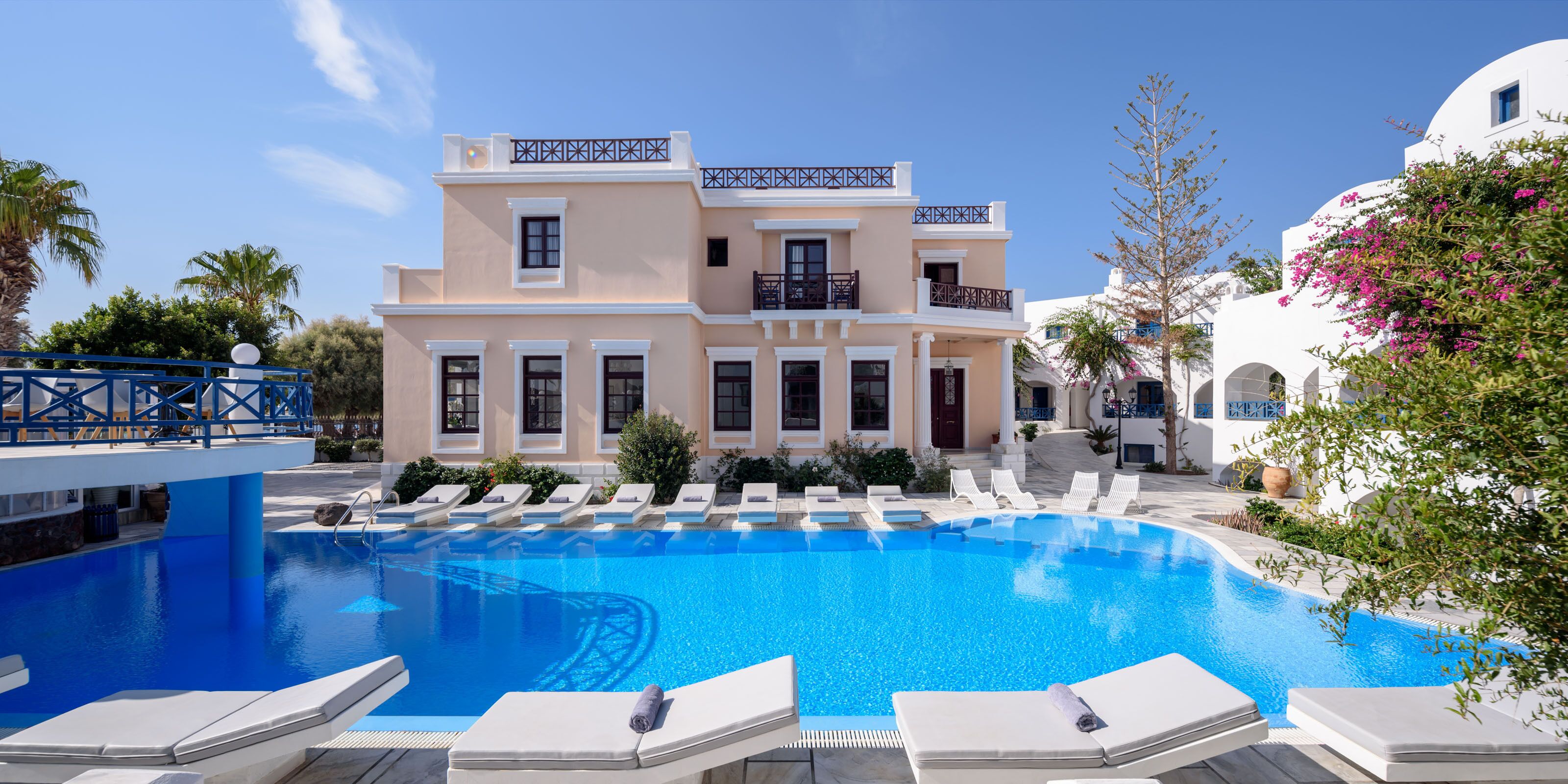 A pool area with lounge chairs, a building with balconies, and a clear blue sky.