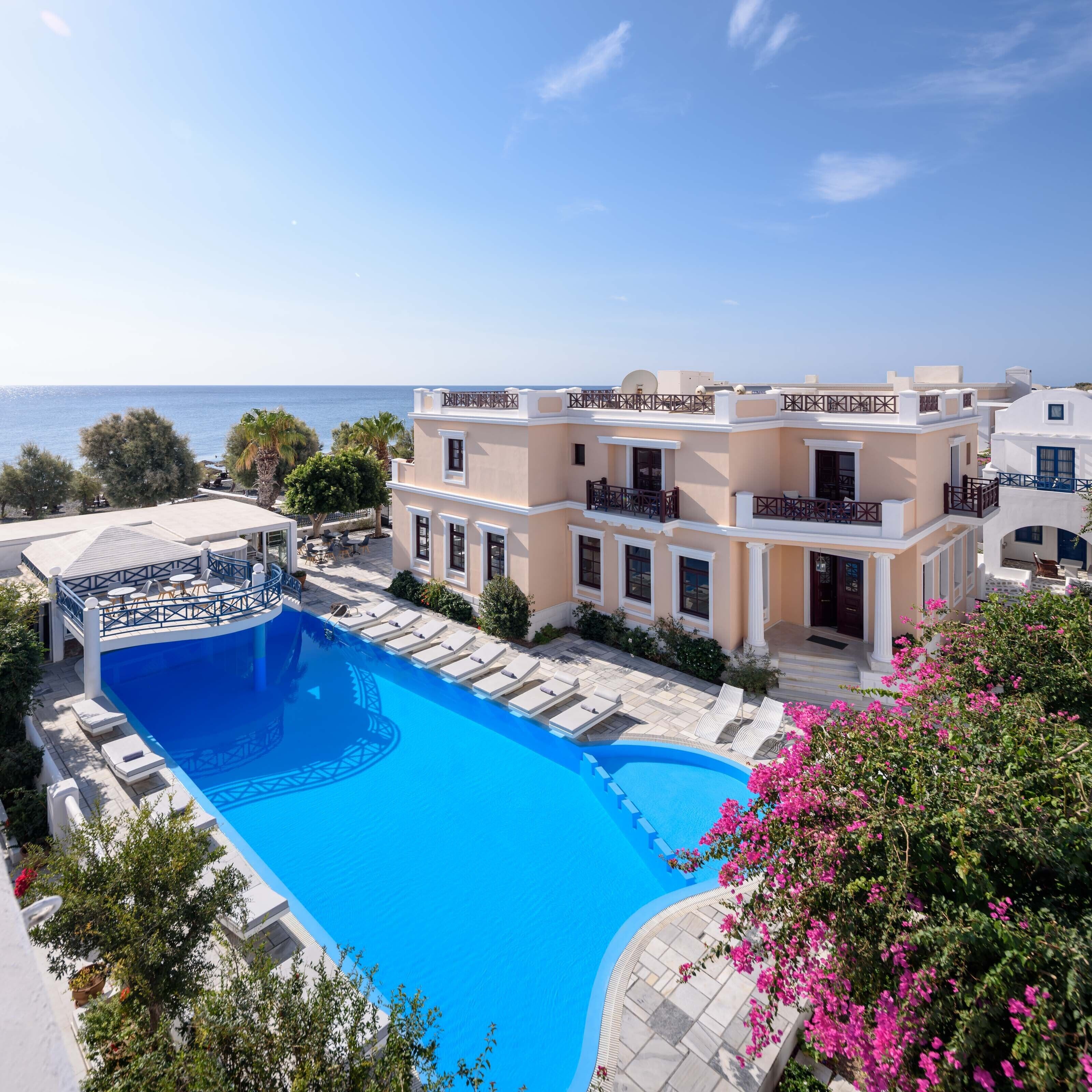 Une grande piscine avec des chaises longues, une vue sur la mer et un immeuble à plusieurs étages doté de balcons.