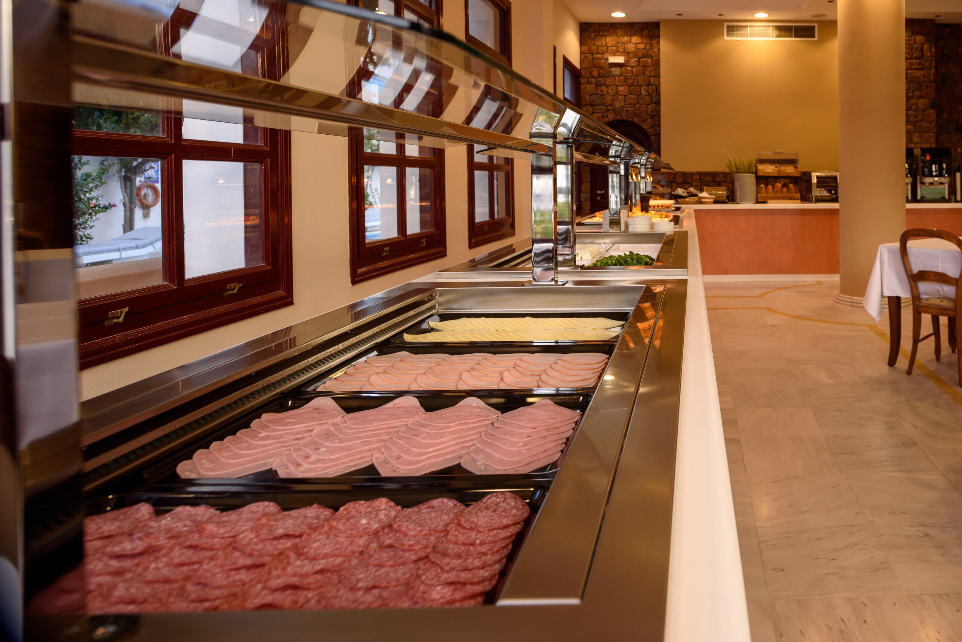 Un buffet proposant différents types de viandes, un comptoir avec une sélection de boissons et une vue sur la rue grâce à de grandes fenêtres.