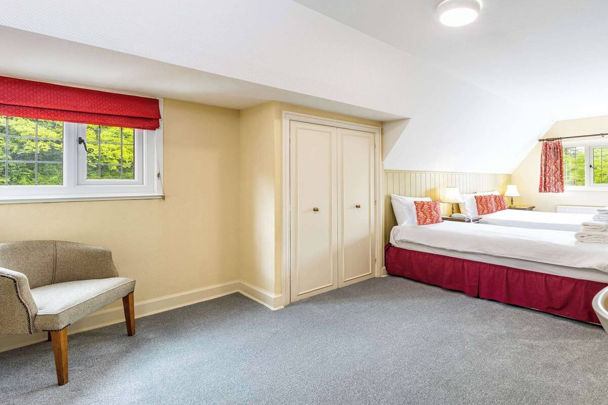 A bedroom with a bed, two bedside tables, a chair, a wardrobe, and a window with a red valance.
