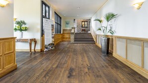 Un hall d’hôtel avec un plancher en bois, un comptoir d’accueil, un escalier et un mur en pierre.