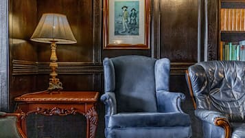 A room with a blue armchair, a wooden side table with a lamp, and a framed picture on the wall.