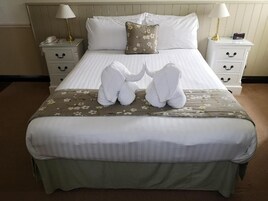 Una cama bien hecha con sábanas blancas, una colcha de estampado floral y dos toallas dispuestas en forma de corazón sobre la cama.