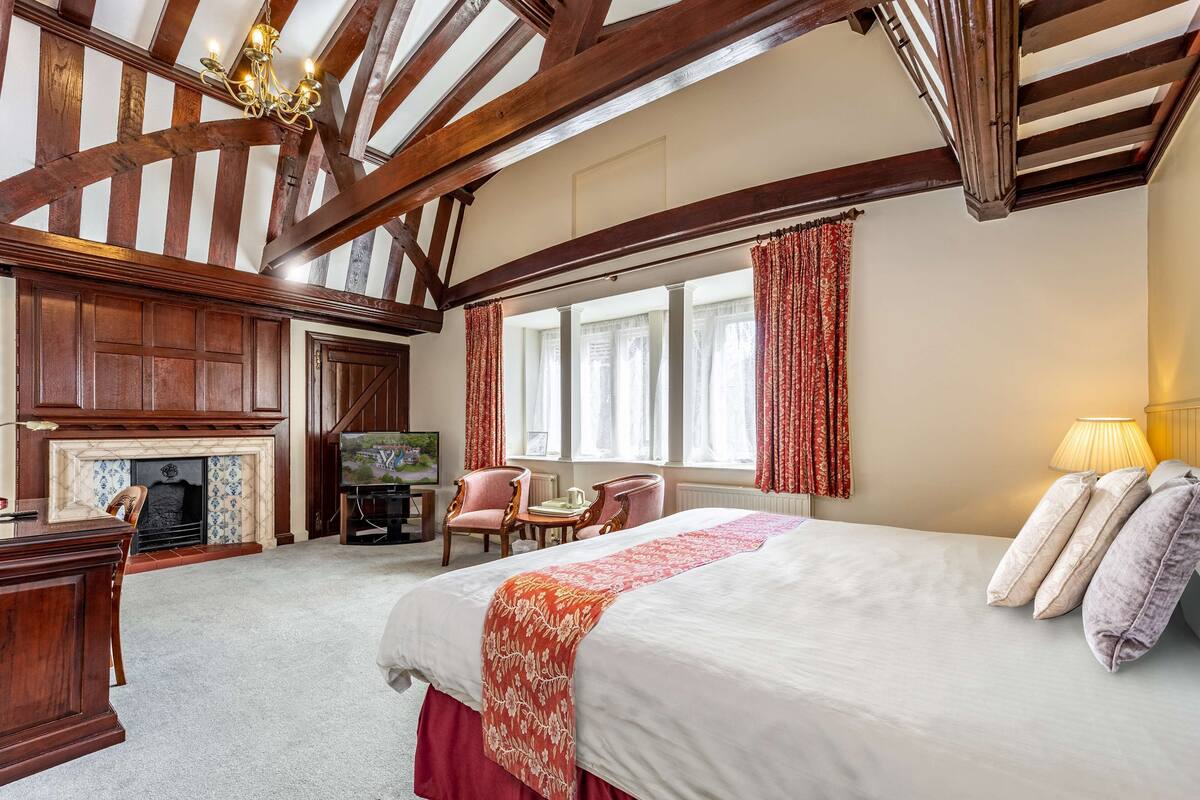 A spacious bedroom with a large bed, a fireplace, a television, and a cozy seating area.