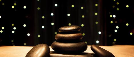 A stack of smooth, polished stones on a wooden surface with a dark background featuring bokeh lights.
