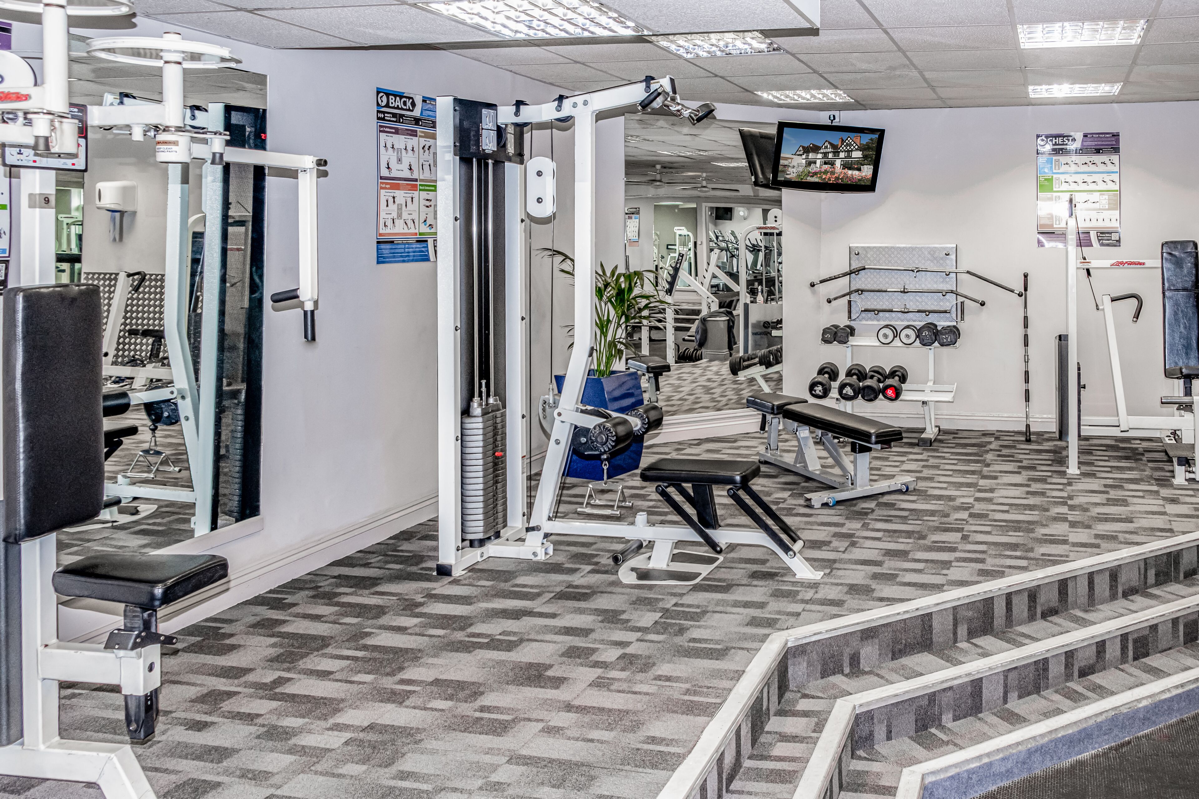 Un gimnasio con diversos equipos de ejercicio, un televisor y un espejo.