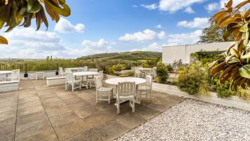 Une terrasse extérieure avec des meubles blancs, un espace recouvert de gravier et une vue sur un paysage vallonné.