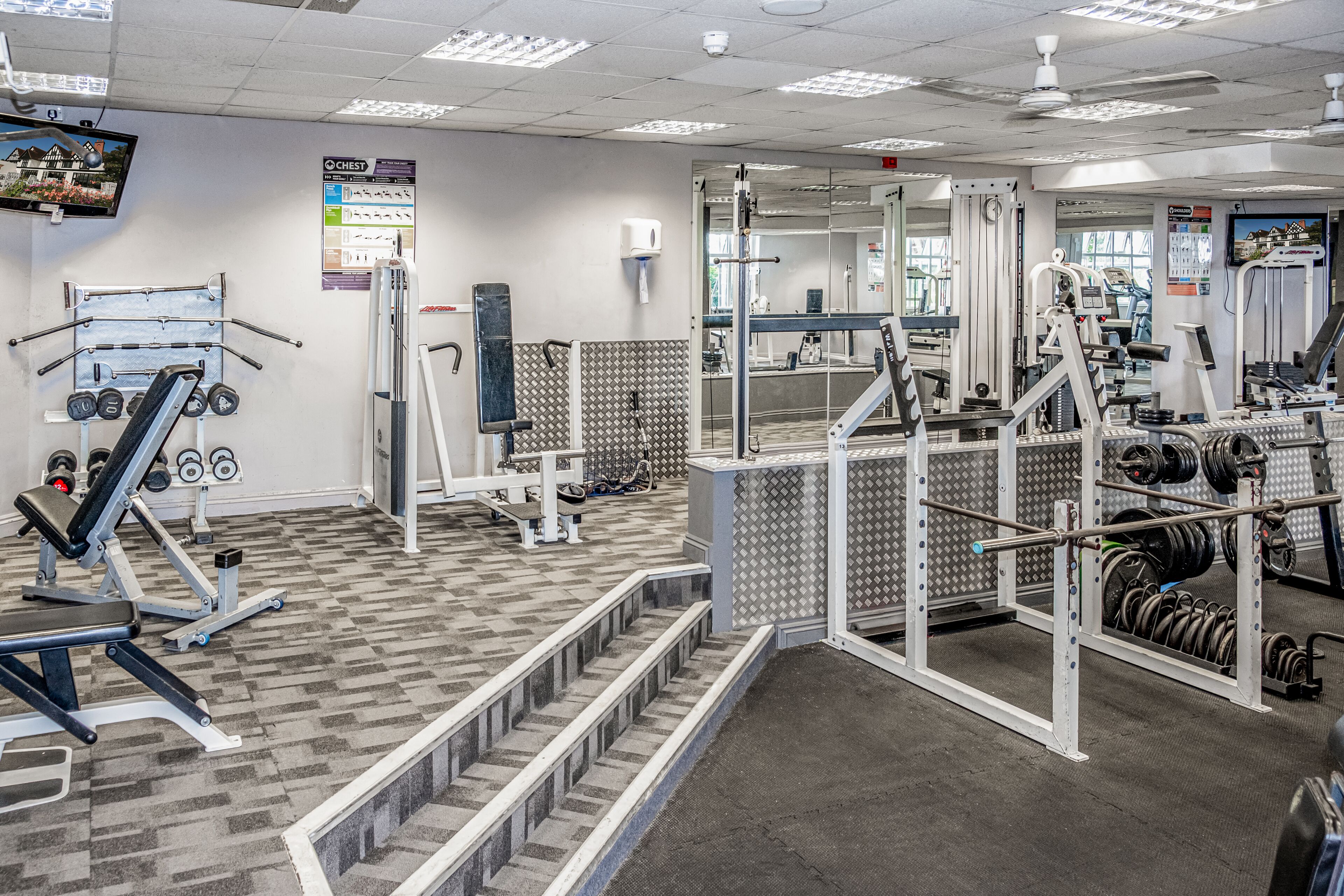 Ein Fitnessstudio mit verschiedenen Trainingsgeräten, darunter Kraftgeräte, Kurzhanteln und Cardiogeräte.