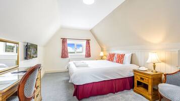 A bedroom with a large bed, a desk with a chair, a nightstand with a lamp, and a window with curtains.