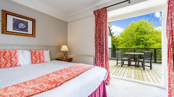 A bedroom with a large bed, a nightstand, a lamp, and a view of an outdoor deck with chairs and a table.