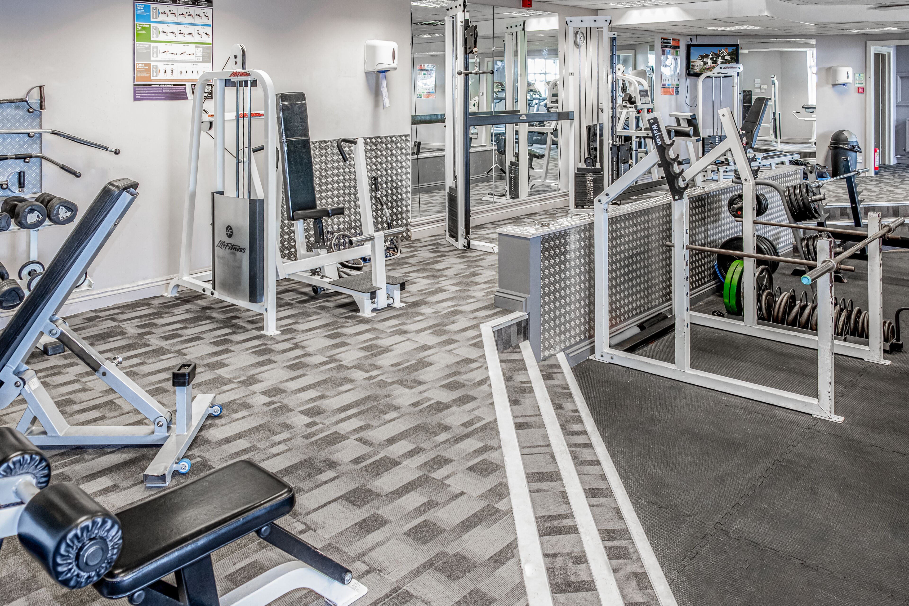 A gym with various exercise equipment, a mirrored wall, and a patterned floor.