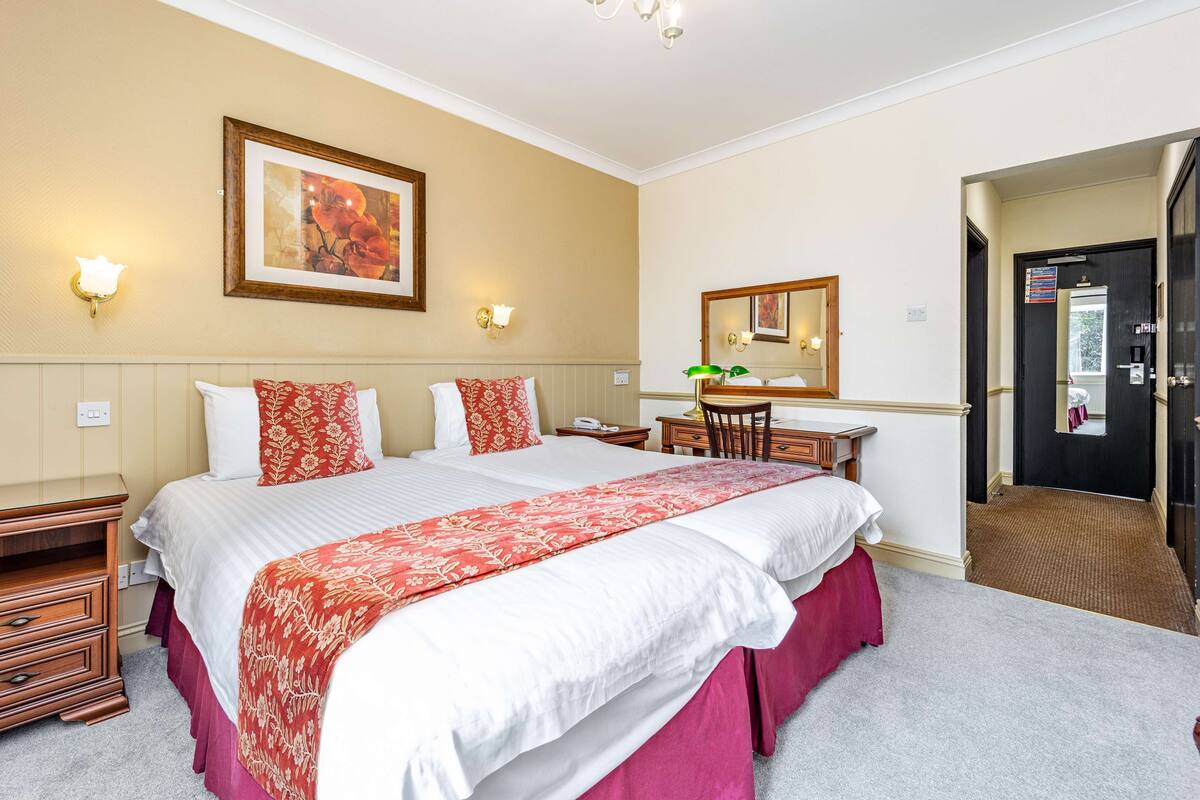 A hotel room with a large bed, a desk, a chair, a mirror, and a door.