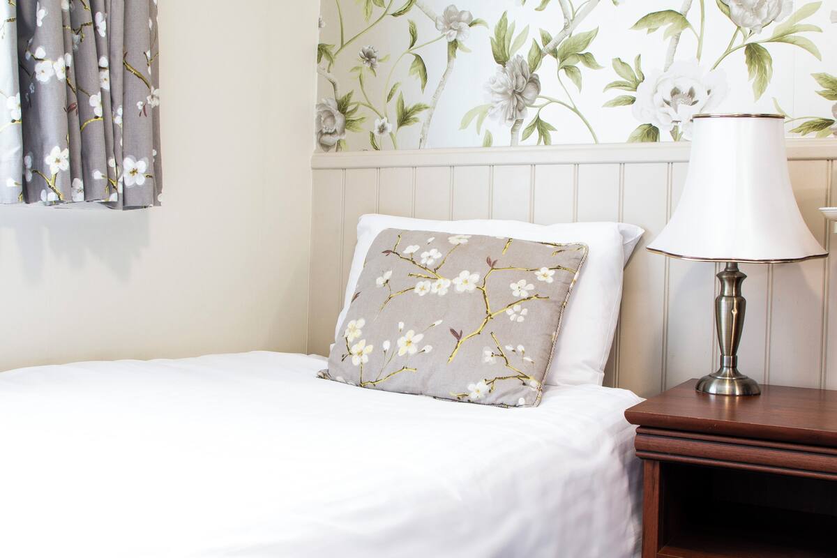 A neatly made bed with a floral pillow, a bedside lamp, and a floral wallpaper.