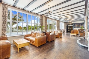 A spacious room with leather sofas, wooden coffee table, large windows, and a high ceiling with exposed beams. - Best Western Webbington Hotel & Spa (Axbridge)