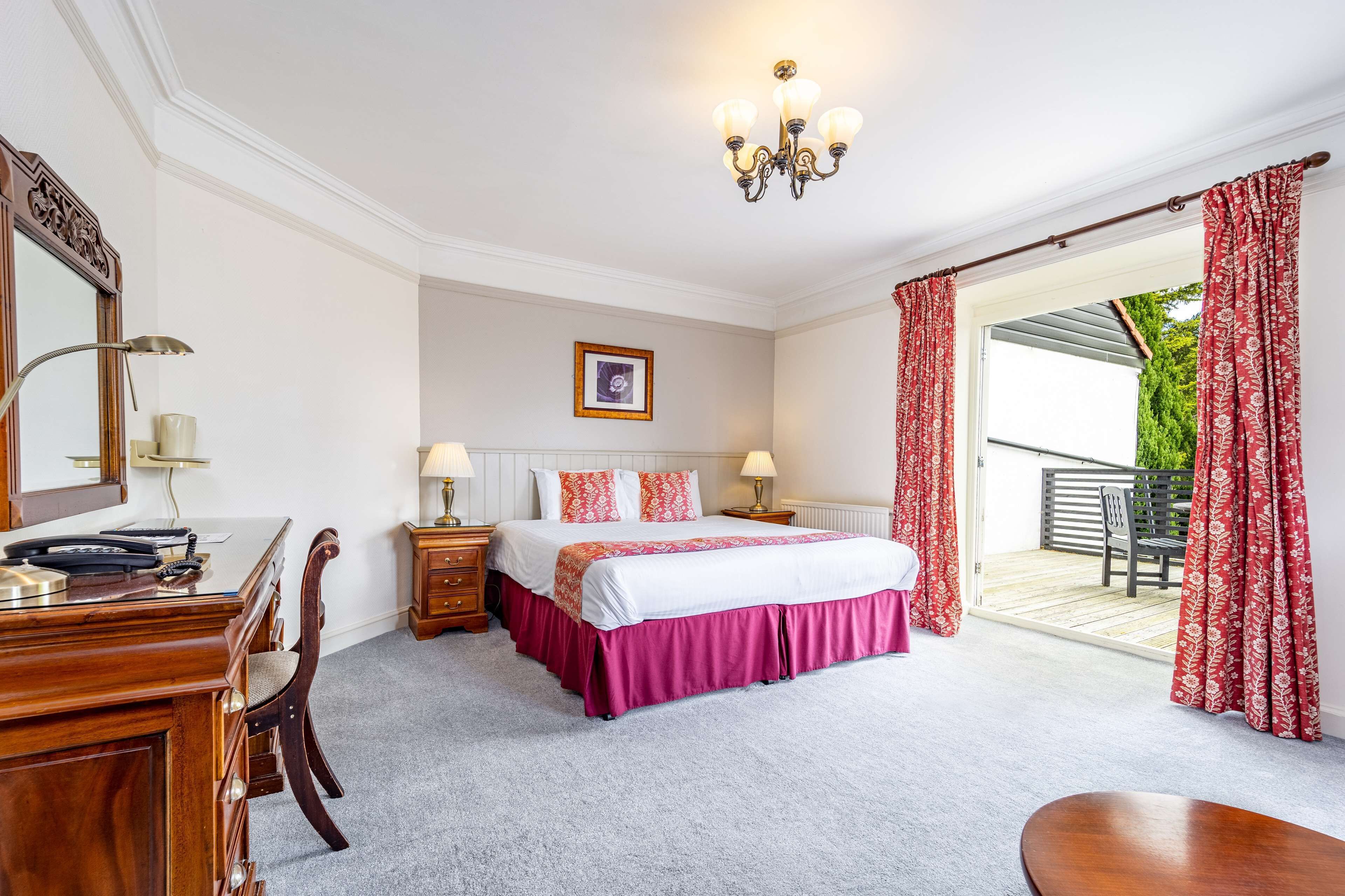 A bedroom with a bed, bedside tables, a desk, and a chair. There is a balcony with a chair and a table.