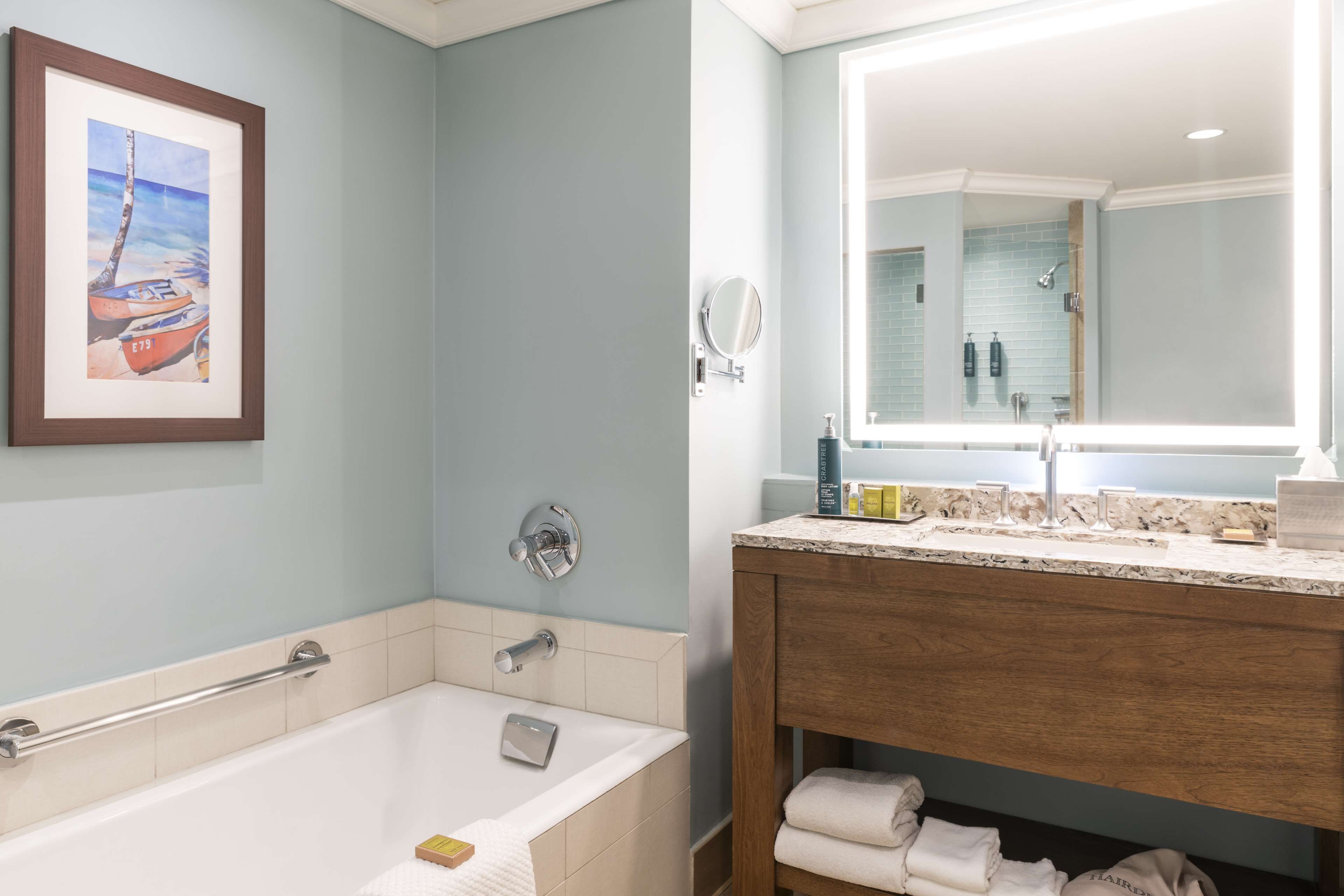 A bathroom with a bathtub, a vanity with a mirror, and a framed picture on the wall.