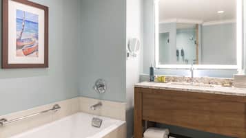 A bathroom with a bathtub, a vanity with a mirror, and a framed picture on the wall.