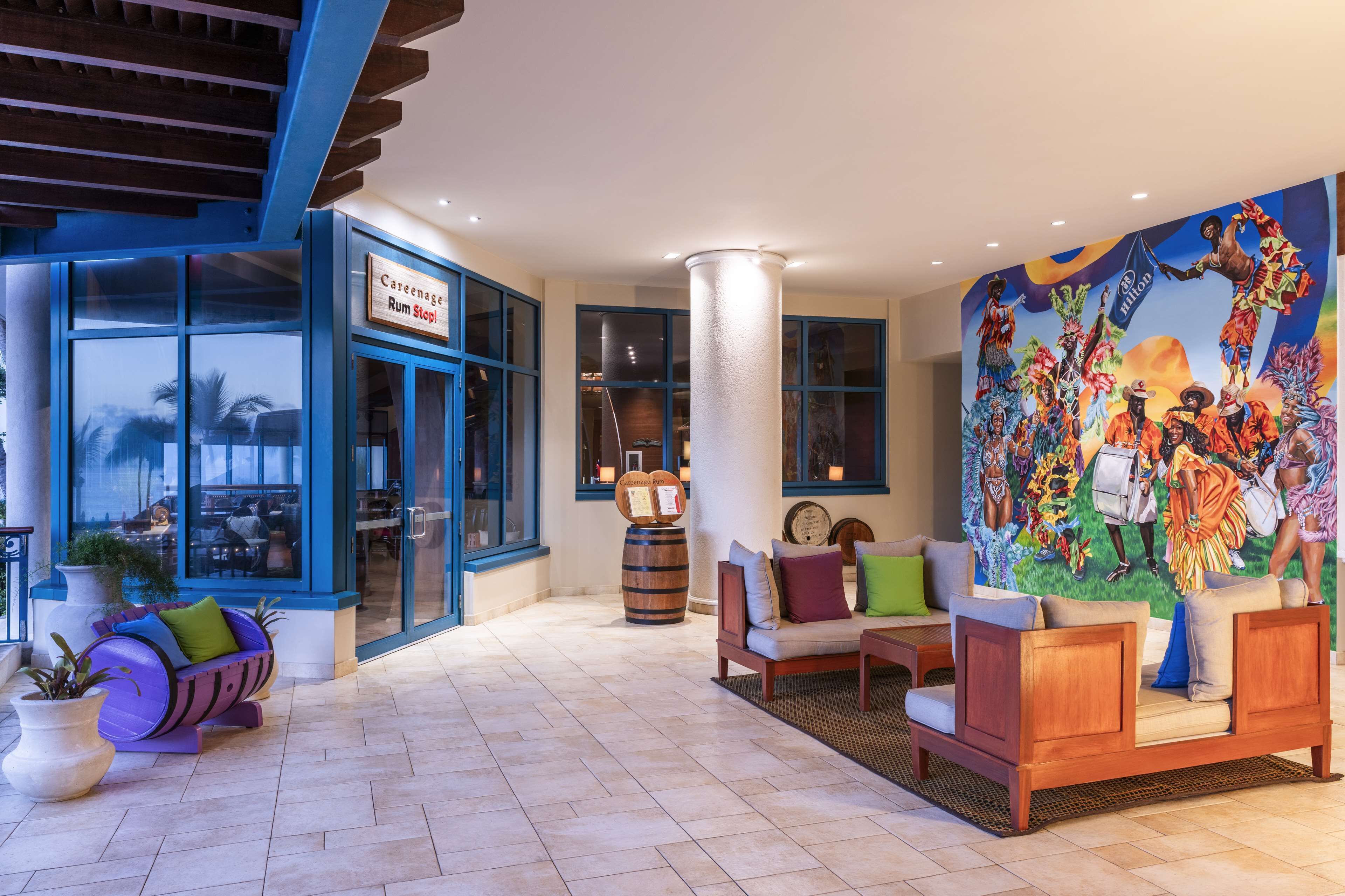 Vestíbulo de hotel con un gran mural, zonas de estar y letrero de una taberna de ron.