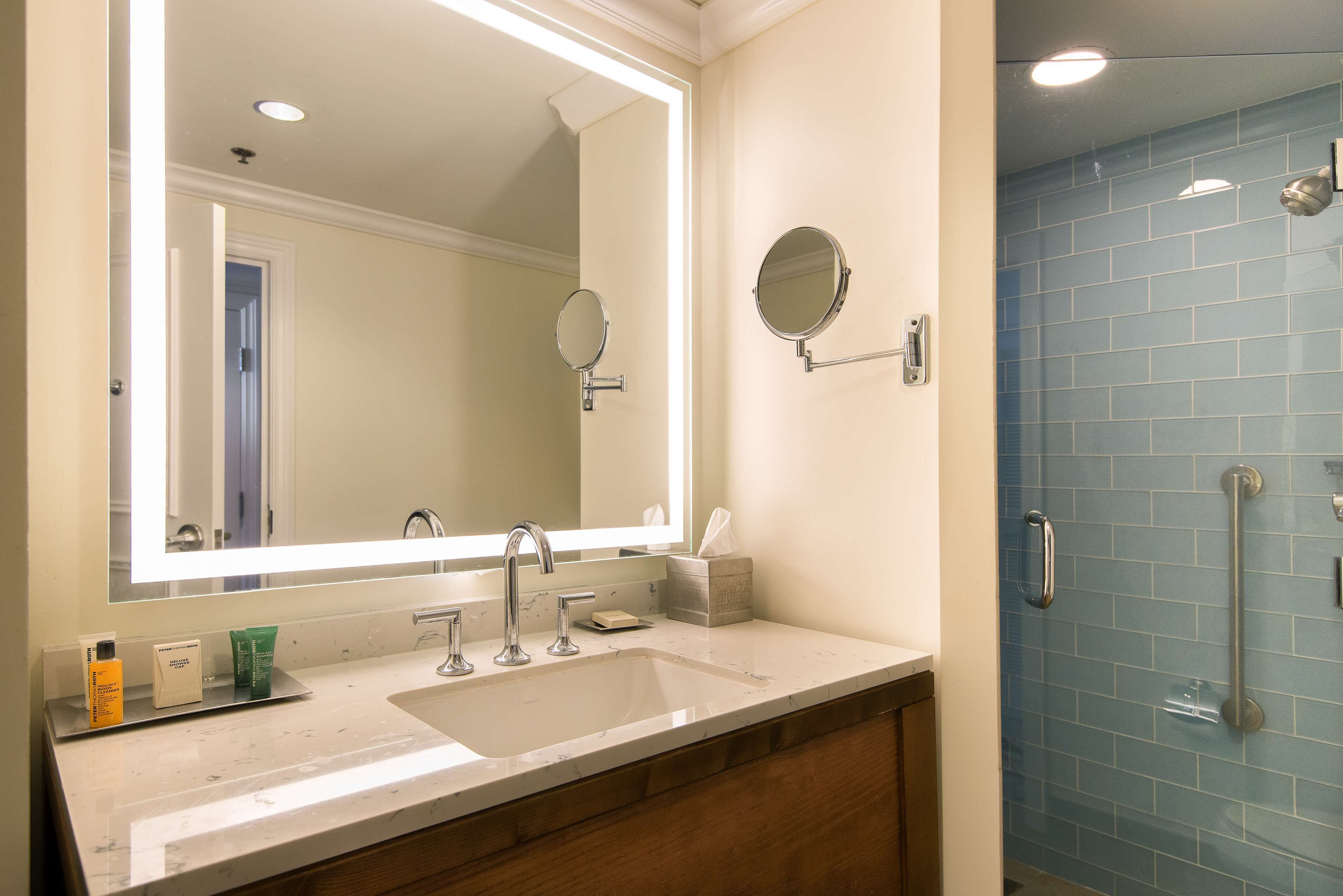 A bathroom with a large mirror, a sink, and a shower with a handrail.