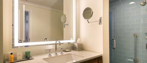 A bathroom with a large mirror, a sink, and a shower with a handrail.