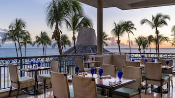 Un restaurante con terraza al aire libre y vistas al mar, con sillas de mimbre y vasos azules.